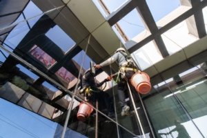 Technicians performing high-rise glass façade cleaning using safety harnesses