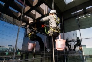 Professional window cleaners suspended by ropes cleaning a glass building façade