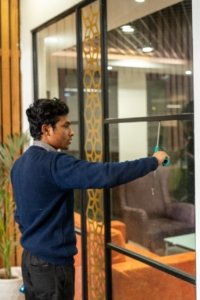 Indoor cleaning staff wiping a glass partition with a squeegee in an office space