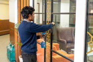 CAS Facilities staff member cleaning an office glass partition with a spray bottle and squeegee.